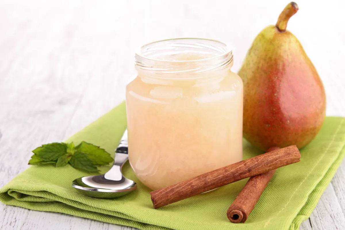 A jar of baby food beside a pear and a cinnamon stick
