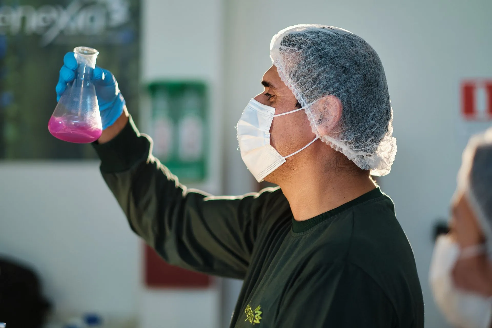 A laboratory technician holding up a flask of pink solution