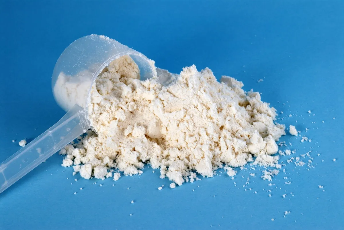 A scoop of protein powder spilling onto a blue surface