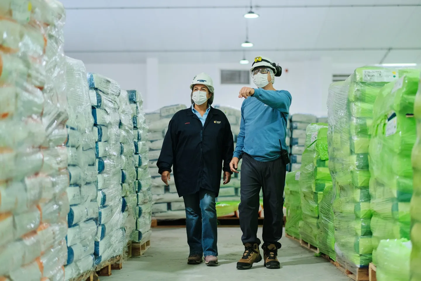 Two workers walking a warehouse aisle stacked with labelled sacks